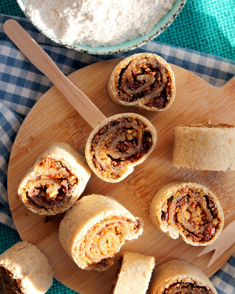 Piccoli salatini mediterranei fatti in casa, a forma di spirale, serviti su un piccolo tagliere di legno, visti dall'alto