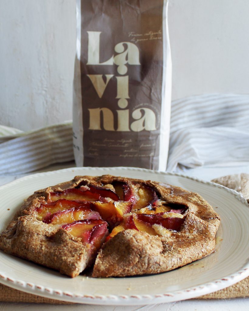 La confezione da kg della farina Lavinia integrale e un piatto beige che contiene una gallette dolce farcita con pesche e mandorle.
